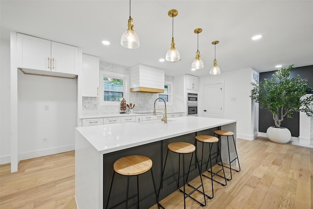 kitchen with double oven, baseboards, light wood-type flooring, white cabinetry, and a sink