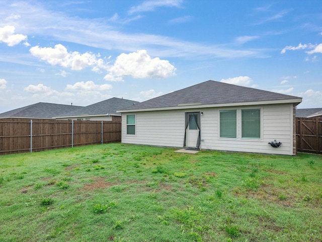 rear view of house featuring a lawn, a shingled roof, and a fenced backyard