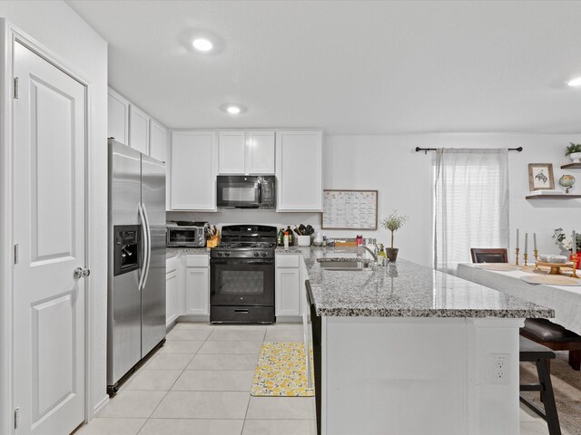 kitchen featuring a sink, light tile patterned floors, black appliances, a peninsula, and white cabinetry
