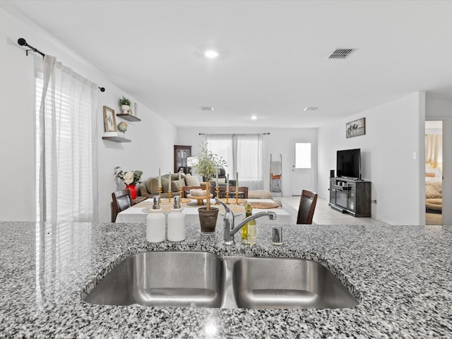 kitchen featuring a sink, open floor plan, stone counters, and visible vents
