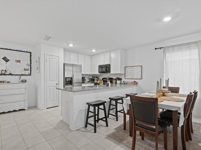 kitchen with light stone countertops, black microwave, a peninsula, stainless steel refrigerator with ice dispenser, and visible vents