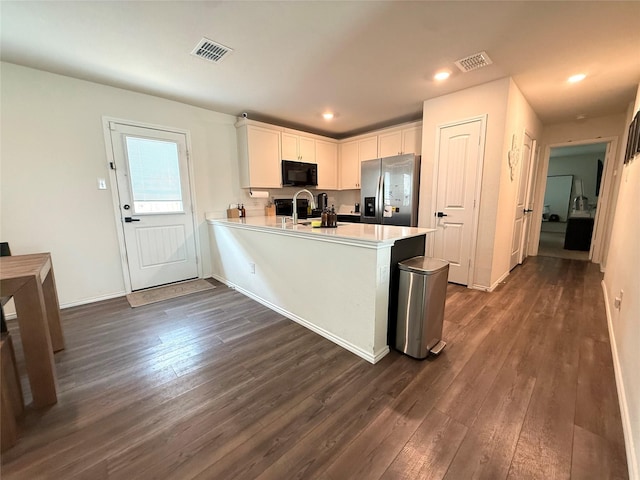 kitchen with black microwave, stainless steel fridge, visible vents, and dark wood-type flooring