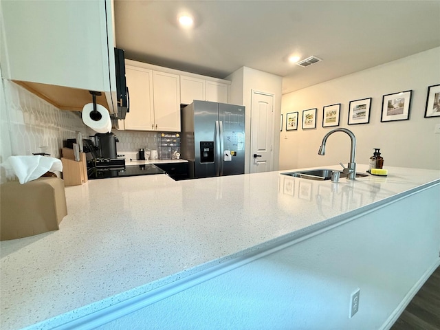 kitchen with visible vents, stainless steel fridge, light stone counters, a sink, and backsplash