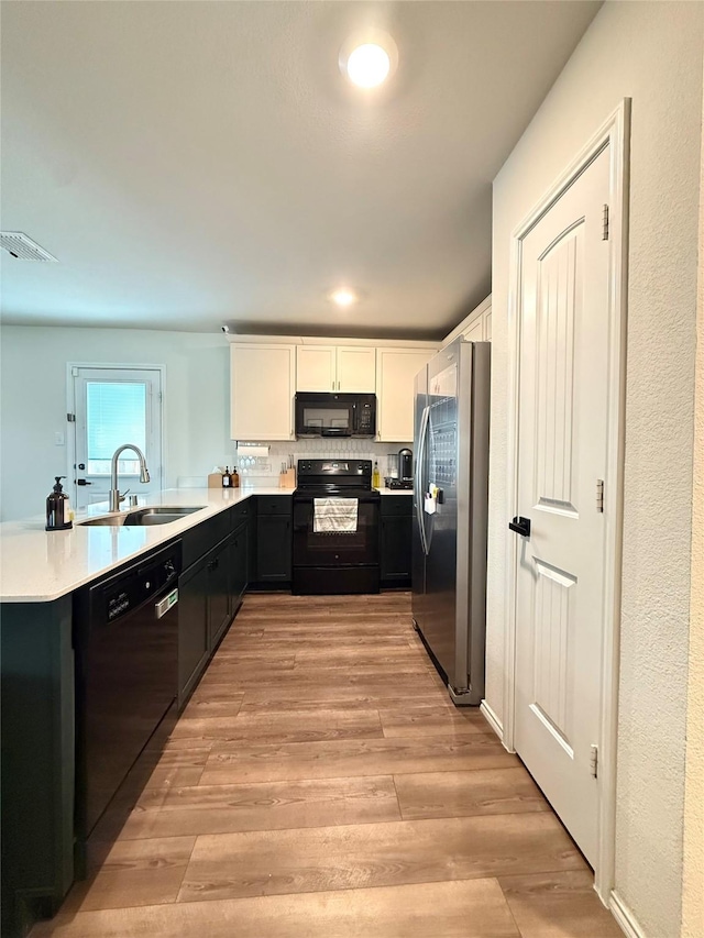 kitchen with a sink, white cabinetry, black appliances, and light wood-style flooring