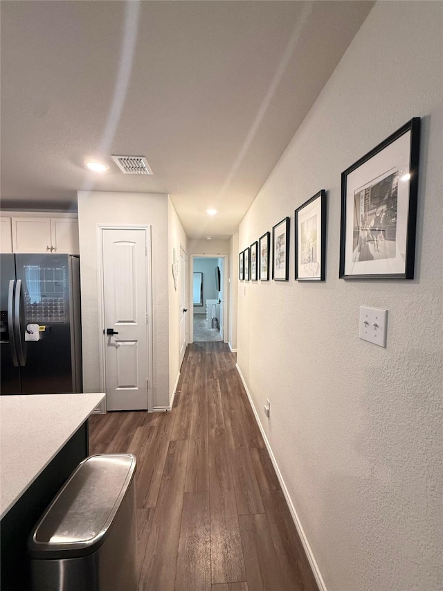 hall with baseboards, a textured wall, dark wood finished floors, and visible vents