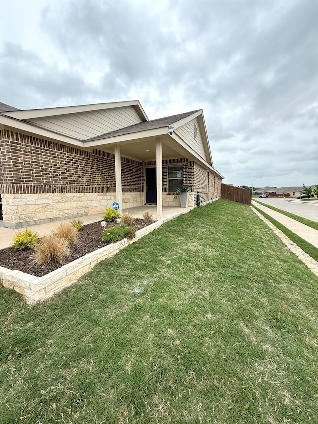 view of property exterior with brick siding, a lawn, fence, and a patio area