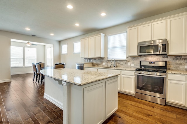 1130 Pasatiempo Dr, Frisco, TX 75036 - kitchen with appliances with stainless steel finishes, a sink, a kitchen island, decorative backsplash, and dark wood-style floors