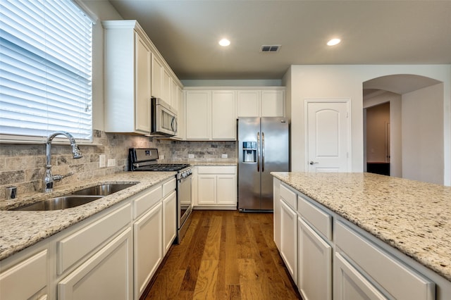 1130 Pasatiempo Dr, Frisco, TX 75036 - kitchen featuring stainless steel appliances, a sink, dark wood-style flooring, arched walkways, and decorative backsplash