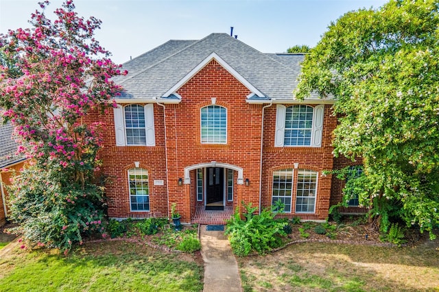 view of front of property featuring brick siding, a front lawn, and roof with shingles