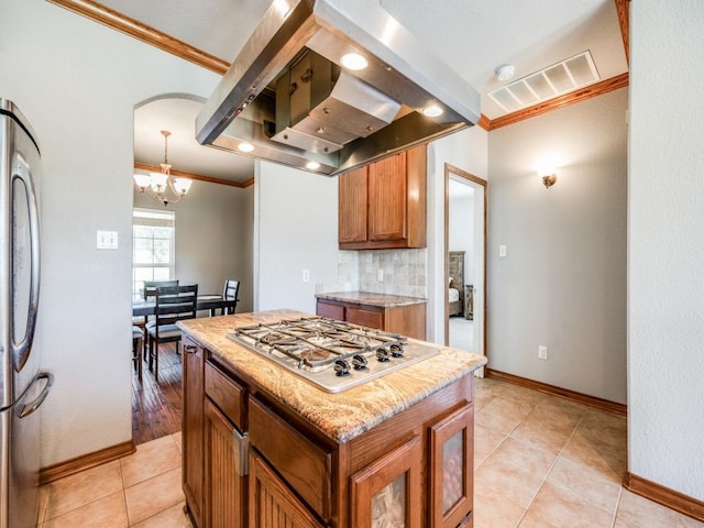 kitchen with brown cabinetry, ornamental molding, island range hood, a notable chandelier, and stainless steel appliances