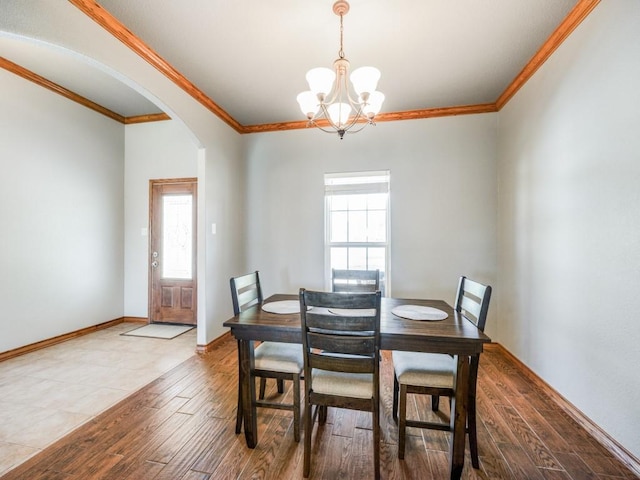 dining area with arched walkways, an inviting chandelier, ornamental molding, and wood finished floors