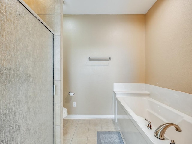 full bath featuring tile patterned floors, baseboards, a garden tub, and toilet