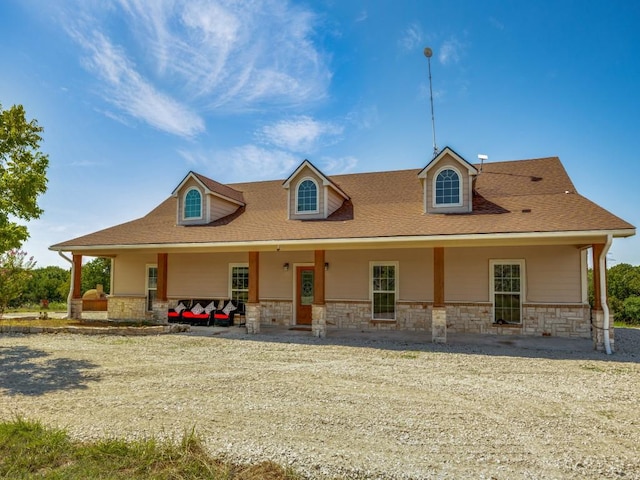 farmhouse inspired home featuring roof with shingles, covered porch, and stone siding