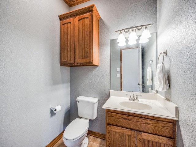 bathroom with vanity, baseboards, a textured wall, and toilet