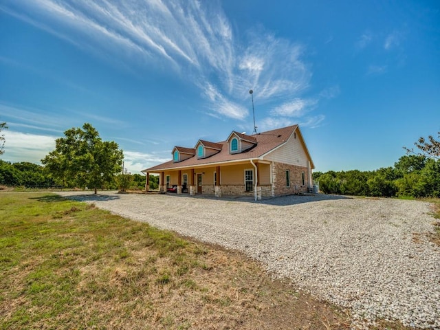 back of house featuring covered porch, stone siding, and gravel driveway