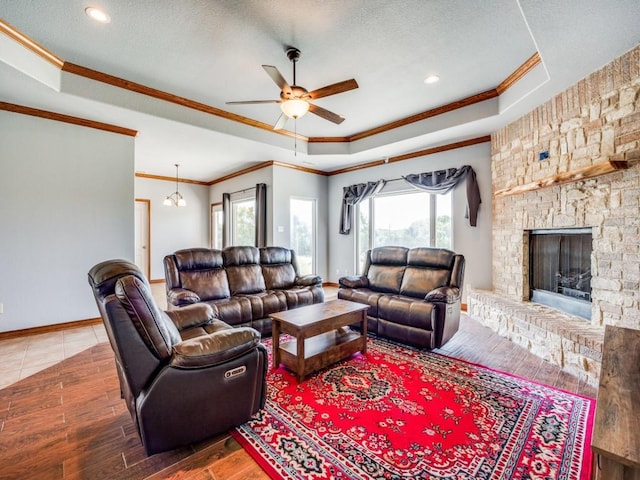 living area featuring a fireplace, a textured ceiling, ceiling fan with notable chandelier, a tray ceiling, and ornamental molding