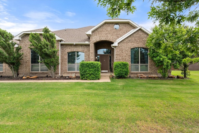 single story home featuring roof with shingles, brick siding, and a front yard
