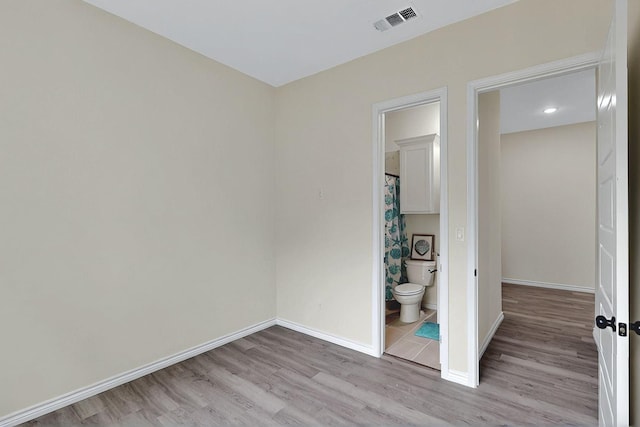 unfurnished bedroom with baseboards, light wood finished floors, connected bathroom, and visible vents