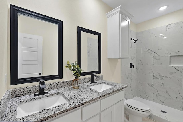 bathroom featuring a sink, a tile shower, toilet, and double vanity