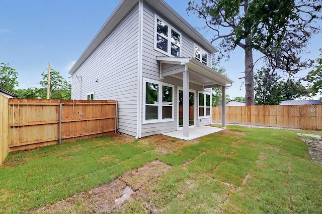 rear view of house with a fenced backyard, a yard, and a patio area