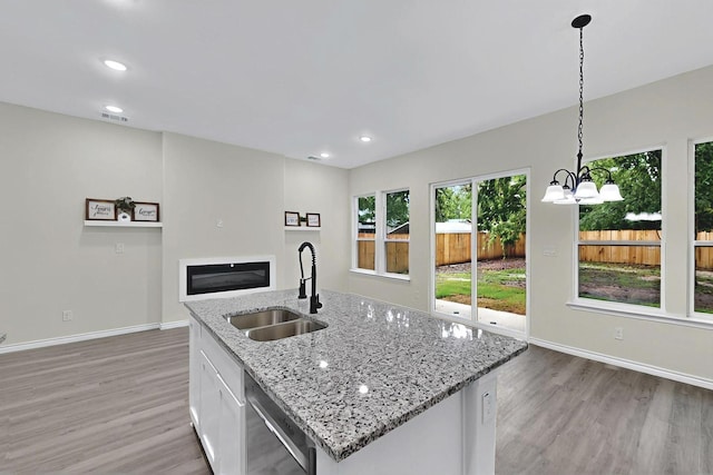 kitchen with stainless steel dishwasher, baseboards, light wood-type flooring, a sink, and decorative light fixtures