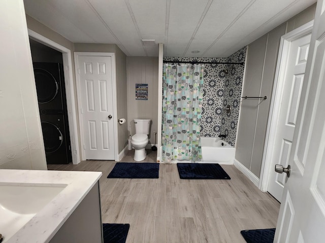 bathroom featuring shower / bath combination with curtain, wood finished floors, stacked washing maching and dryer, vanity, and toilet