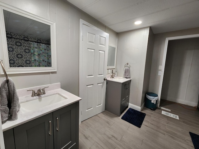 bathroom featuring visible vents, two vanities, a sink, and wood finished floors