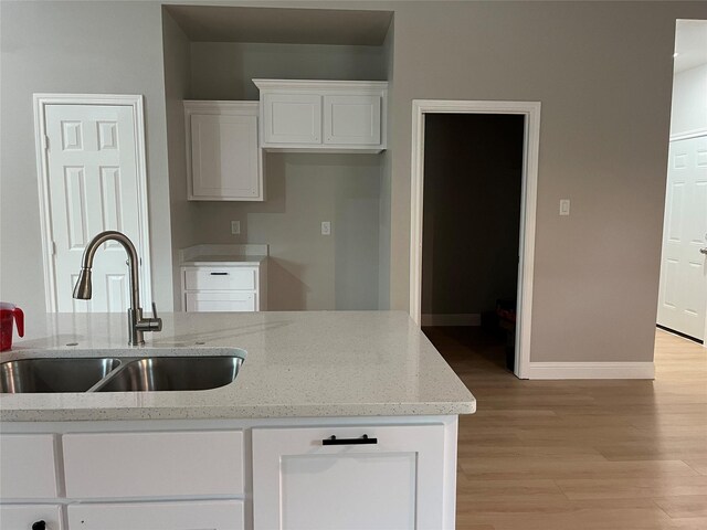 kitchen with baseboards, light wood-type flooring, white cabinets, light stone counters, and a sink