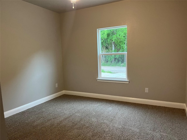 spare room featuring dark colored carpet and baseboards