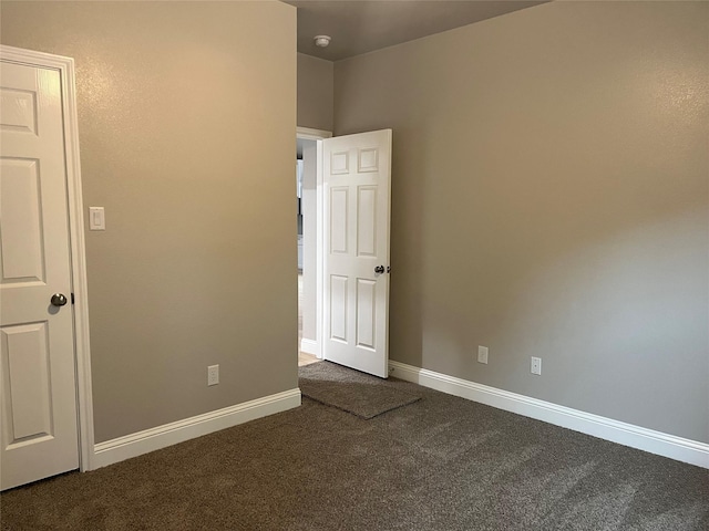 spare room featuring baseboards and dark carpet