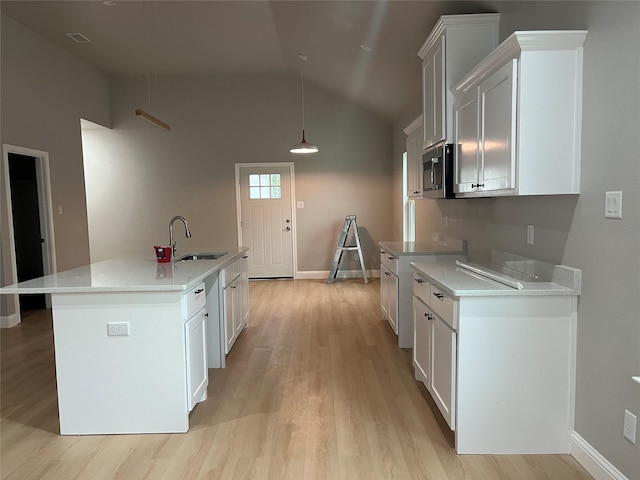 kitchen featuring vaulted ceiling, a sink, stainless steel microwave, light wood finished floors, and white cabinetry