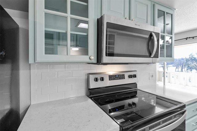 4211 Fairway Dr, Granbury, TX 76049 - kitchen featuring stainless steel appliances, a textured ceiling, tasteful backsplash, glass insert cabinets, and light stone counters