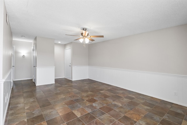 4211 Fairway Dr, Granbury, TX 76049 - empty room featuring ceiling fan, a wainscoted wall, a textured ceiling, and stone finish floors