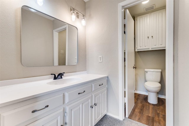bathroom with vanity, toilet, baseboards, wood finished floors, and visible vents