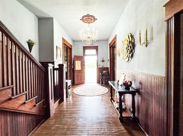 foyer entrance with an inviting chandelier, wainscoting, wood finished floors, and stairway