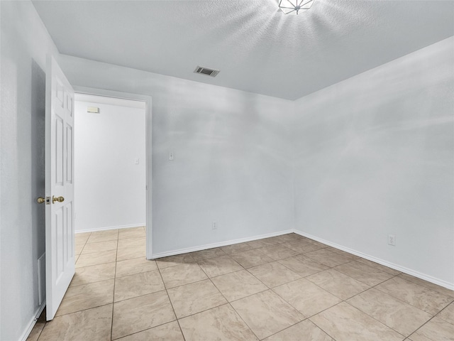 empty room featuring baseboards, a textured ceiling, visible vents, and light tile patterned floors