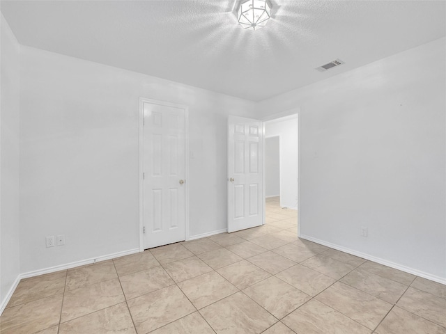 unfurnished bedroom with visible vents, a textured ceiling, baseboards, and light tile patterned floors