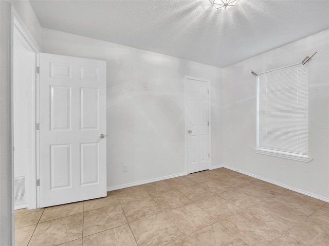 unfurnished bedroom with light tile patterned floors, baseboards, a textured ceiling, and visible vents