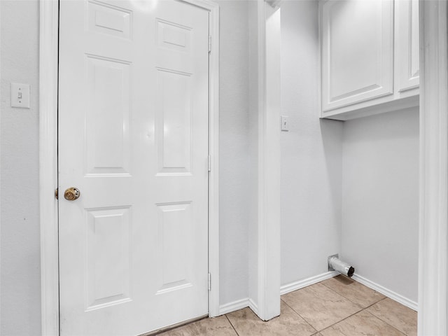 clothes washing area featuring baseboards, cabinet space, and light tile patterned floors