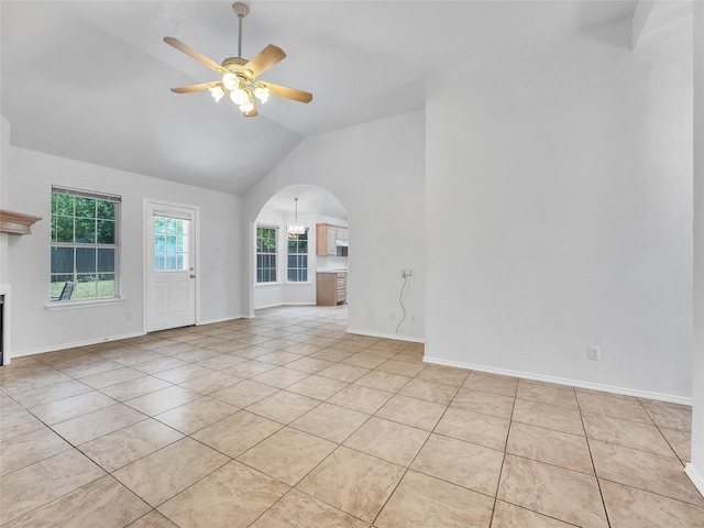 empty room featuring light tile patterned flooring, a fireplace, arched walkways, high vaulted ceiling, and a ceiling fan