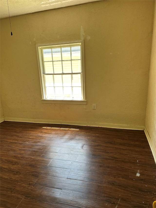 empty room featuring baseboards, a textured wall, and dark wood-style floors