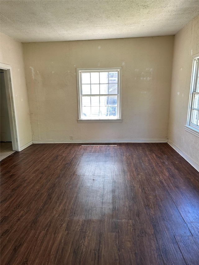 empty room with dark wood-style flooring, a textured ceiling, and baseboards