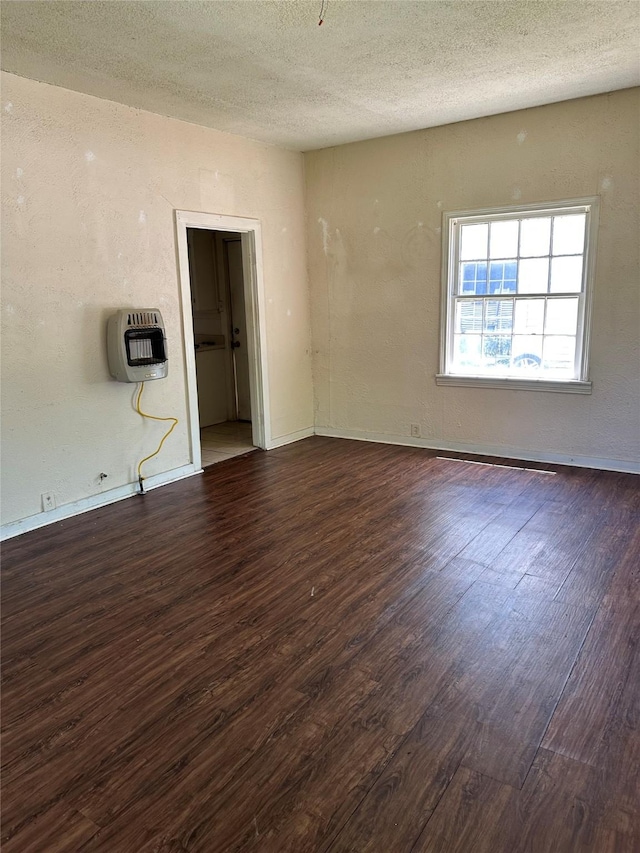 spare room with heating unit, baseboards, a textured ceiling, and dark wood-type flooring