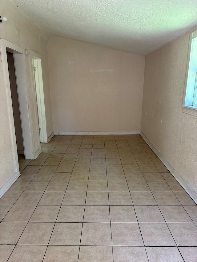 empty room with a textured ceiling and light tile patterned floors