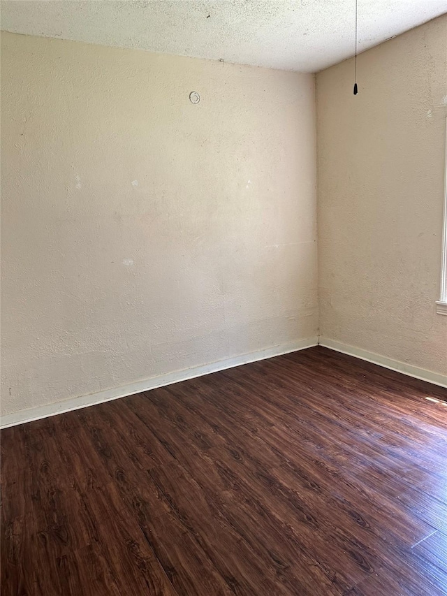 unfurnished room featuring baseboards, a textured wall, and dark wood finished floors
