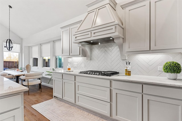 kitchen with an inviting chandelier, premium range hood, tasteful backsplash, vaulted ceiling, and stainless steel gas stovetop