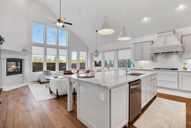 kitchen with light stone countertops, a sink, high vaulted ceiling, open floor plan, and custom range hood