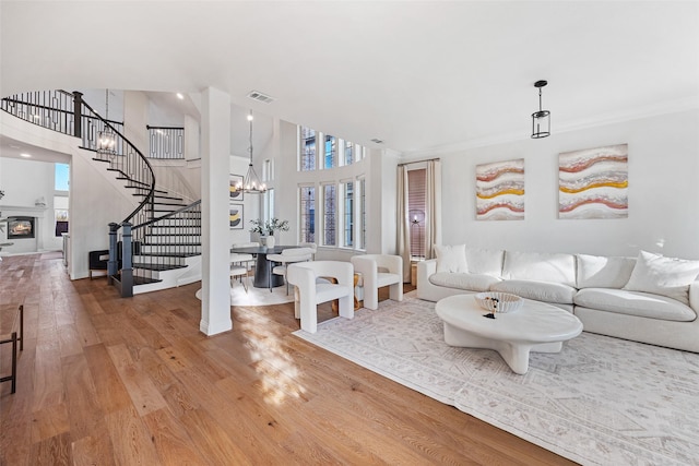 living area with visible vents, wood finished floors, stairway, an inviting chandelier, and a high ceiling