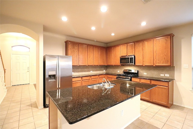 kitchen featuring appliances with stainless steel finishes, a sink, arched walkways, decorative backsplash, and light tile patterned floors