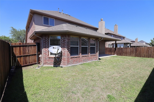 back of house featuring a yard, brick siding, a chimney, and a fenced backyard